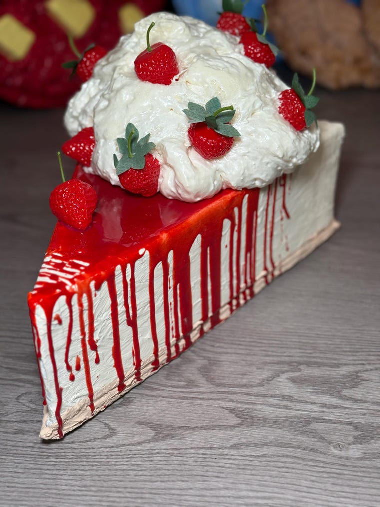 Giant faux strawberry cheesecake slice sculpture with whipped cream and dripping red glaze, handmade by Erynn